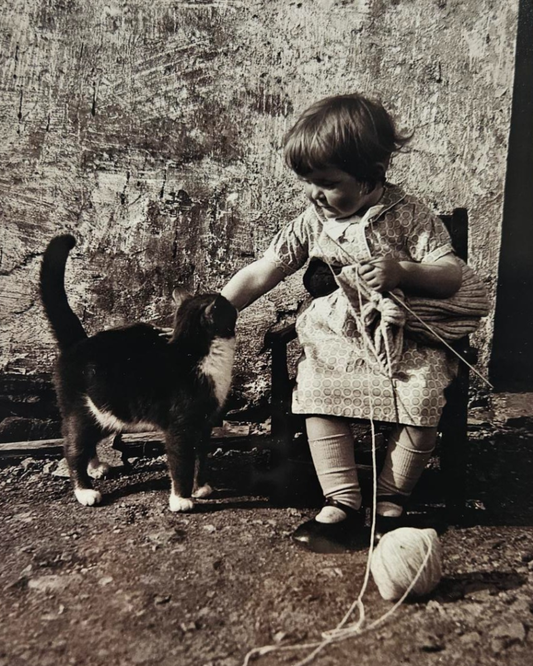 Vintage black and white photo of a child interacting with a cat.